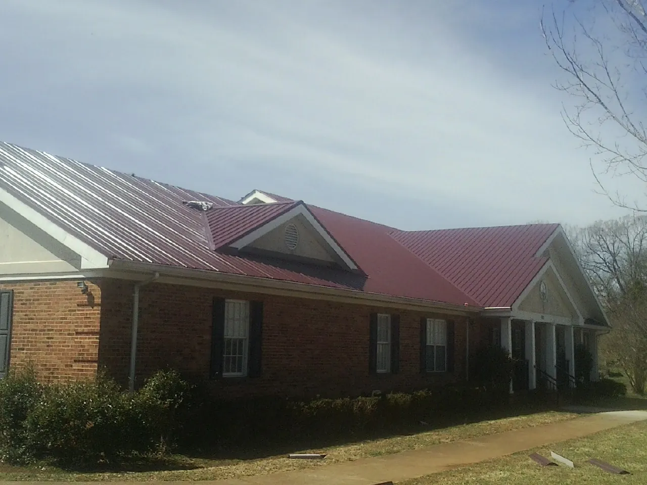 Red metal roof with gabled entries on a long brick building, from a Hail Damage Roof Repair job in Sodus