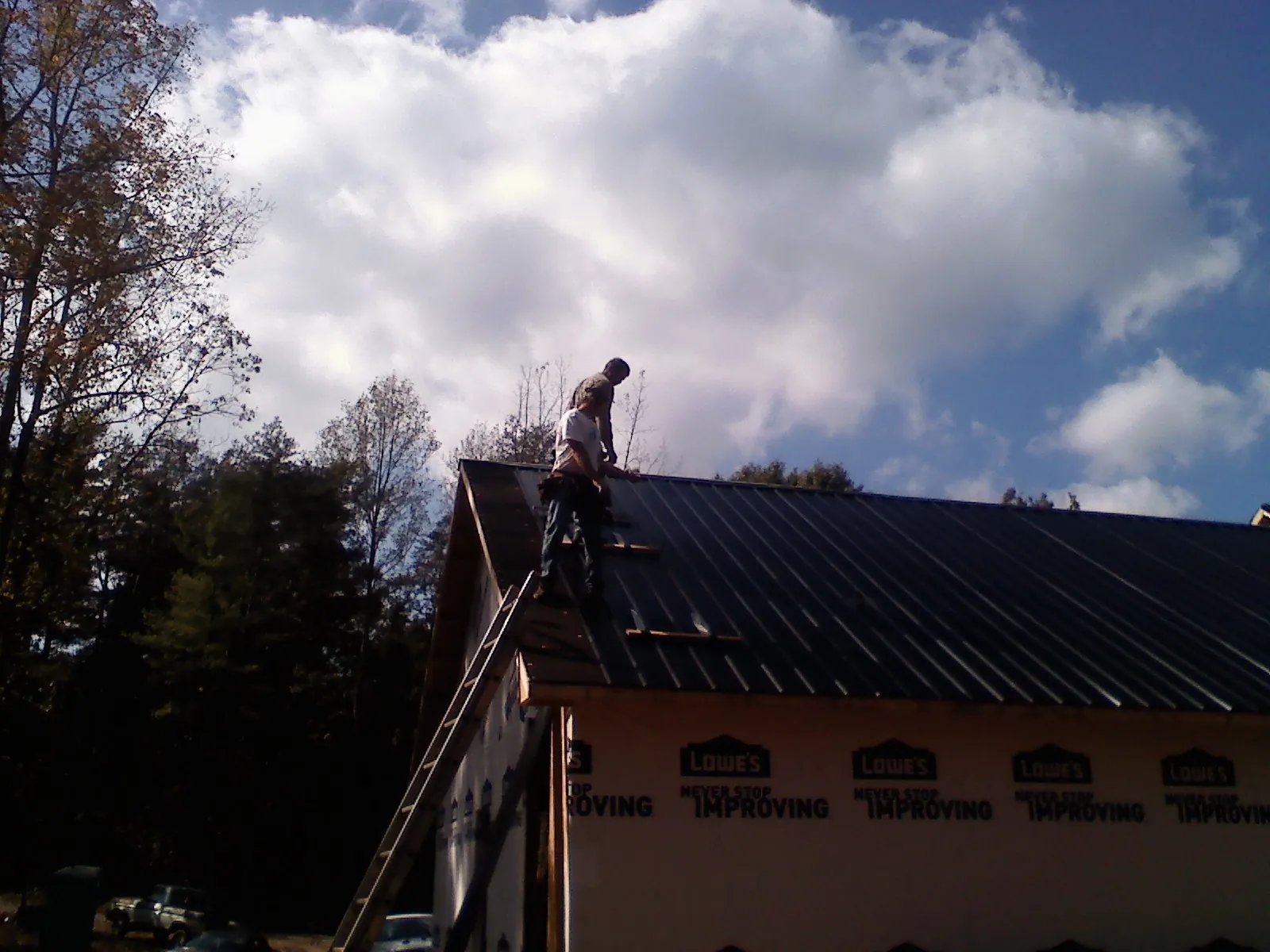 Roofer fastening dark metal panels high against a cloudy sky, from a Roof Inspection job in Sodus