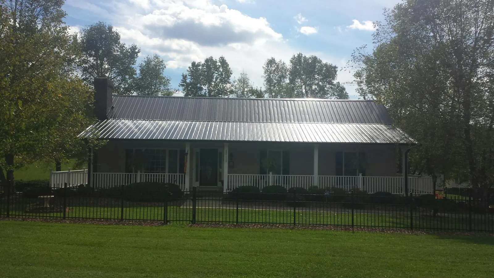 Gray metal roof on a brick ranch with a full width front porch — Gutter Guard Installation work by our crew in Sodus