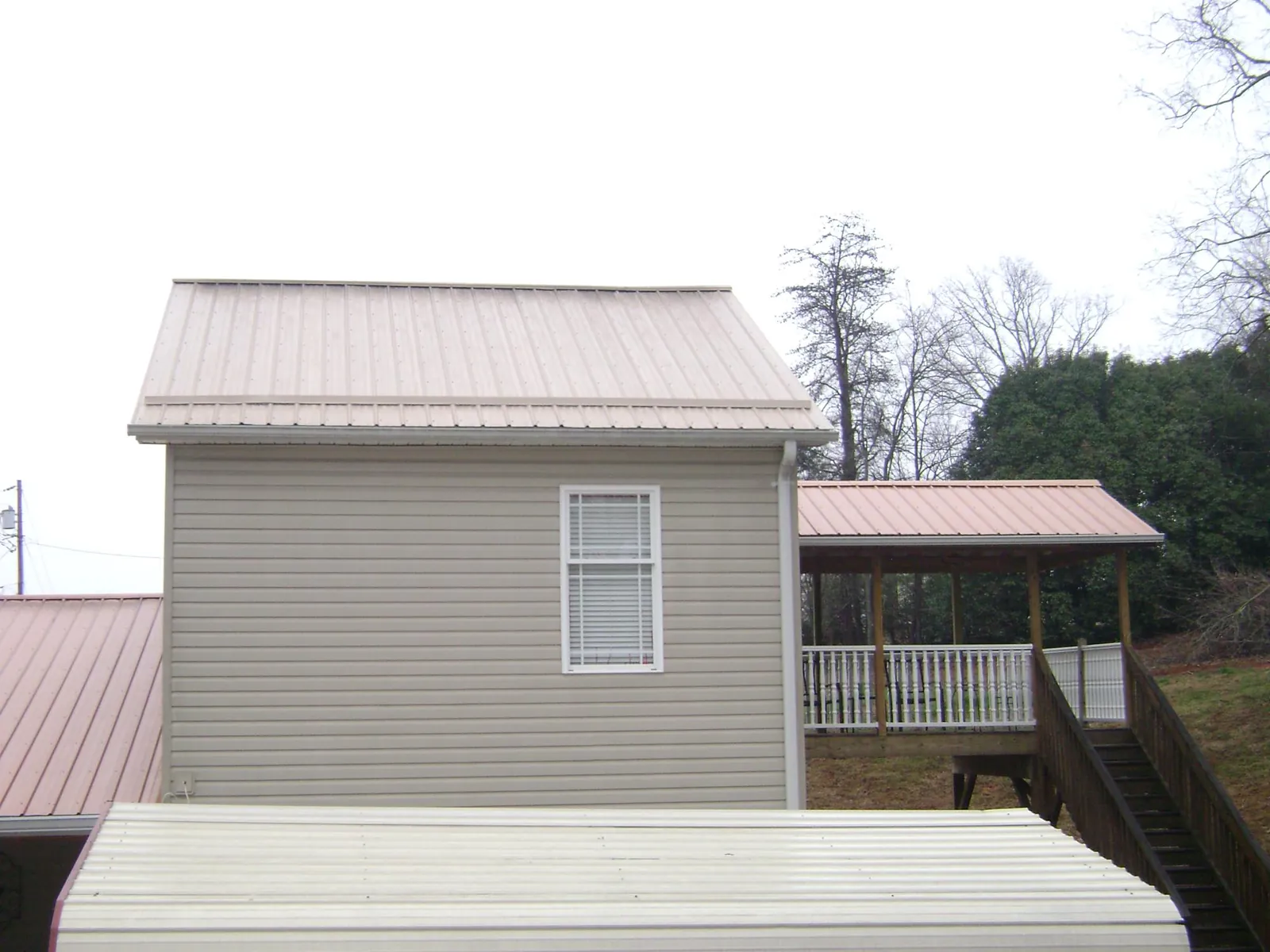 Tan metal roofs on a two story addition and attached porch, from a Roof Replacement job in Sodus